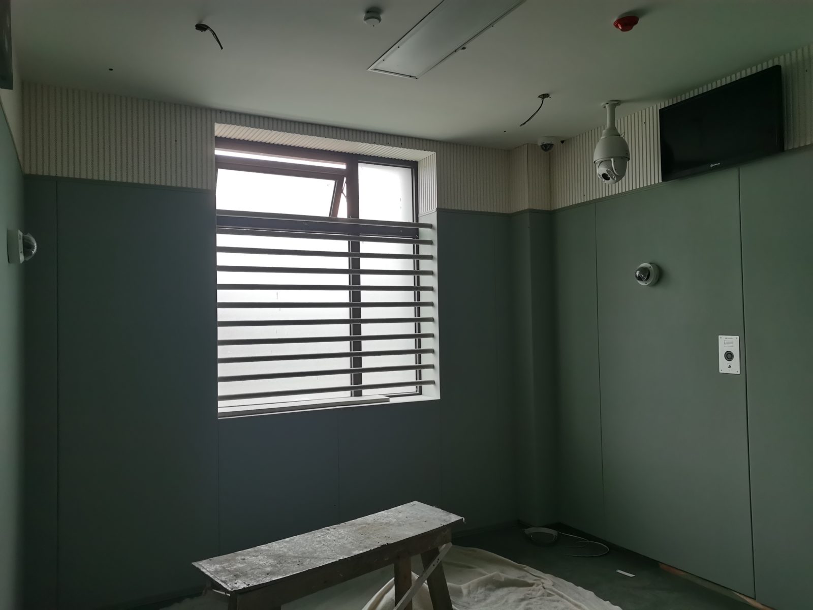 公检法办案区审讯室浅灰色防撞软包墙面装修实景，上部搭配白色穿孔吸音板，防撞防自伤设计