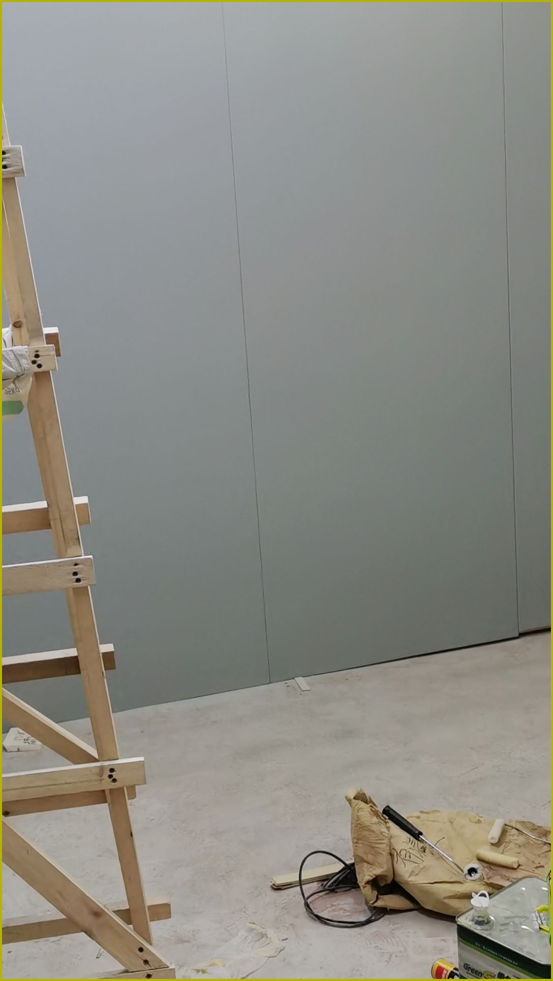 室内声学墙板安装施工现场，大面积灰色平整板材墙面配木制脚手架与施工工具